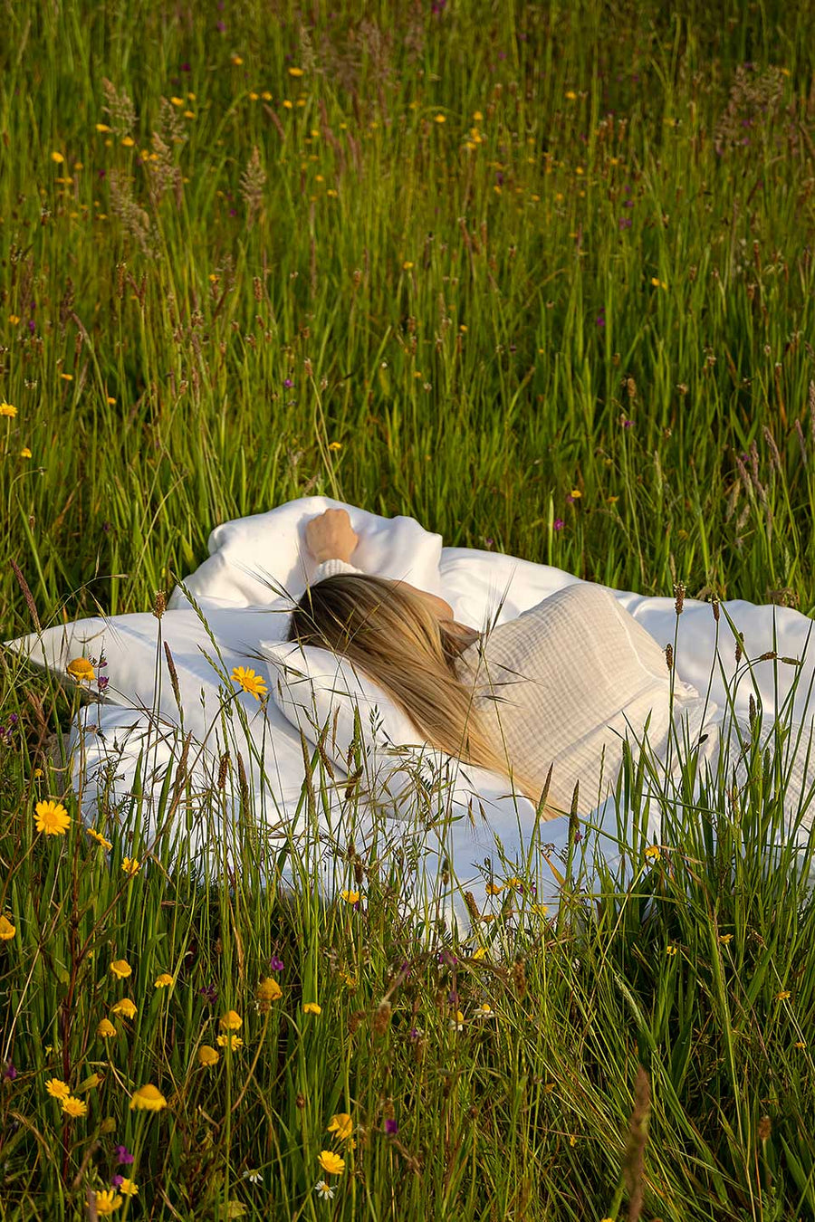 Woman lying in a green field wrapped in a TENCEL™ Lyocell sheet.