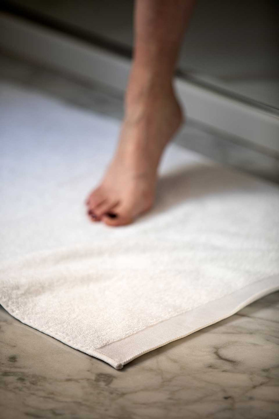 Woman stepping on a white Egyptian Cotton™ Bath Mat.